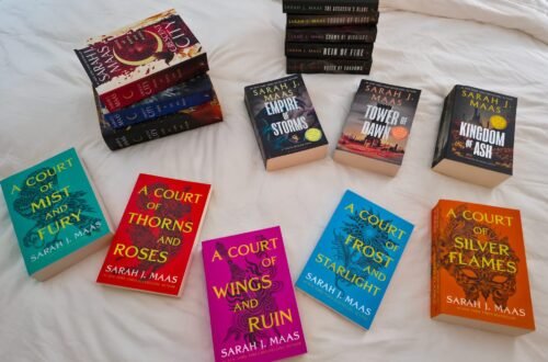 Sarah J. Maas Book Collection on A White Plush Bed Scattered Across