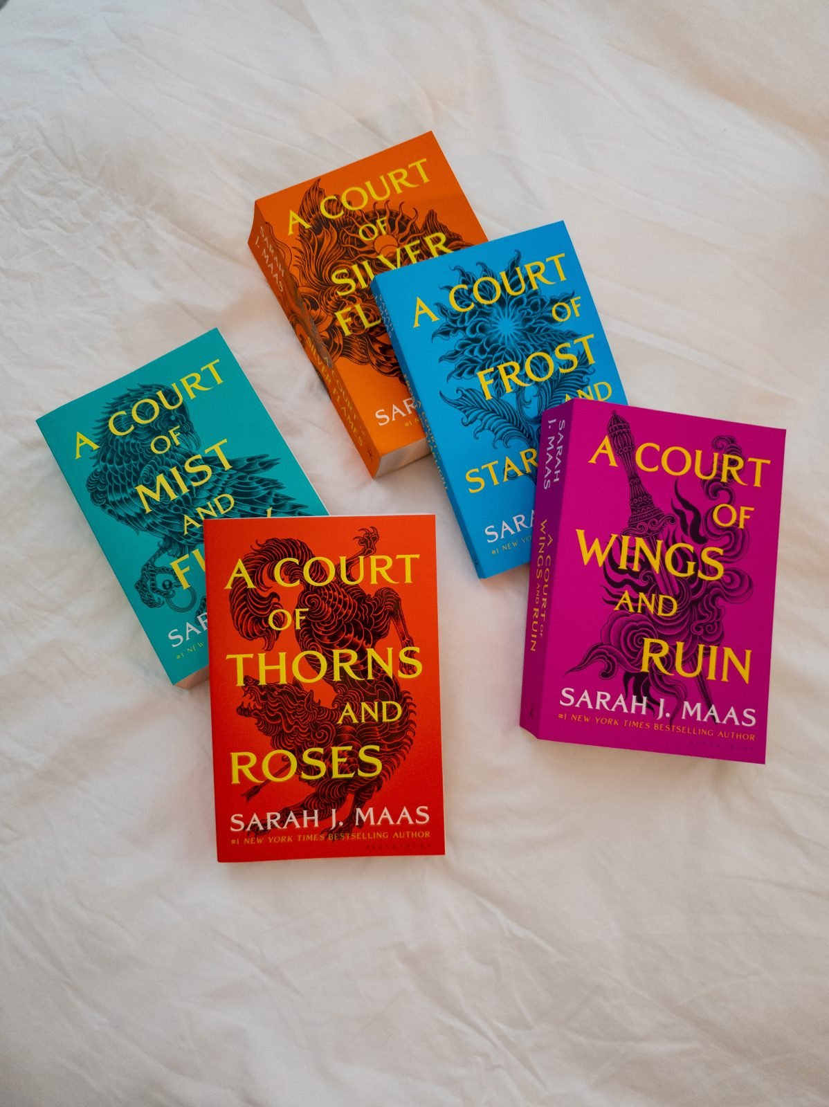 Arielle's A Court of Thorns and Roses paperback set on a white bed