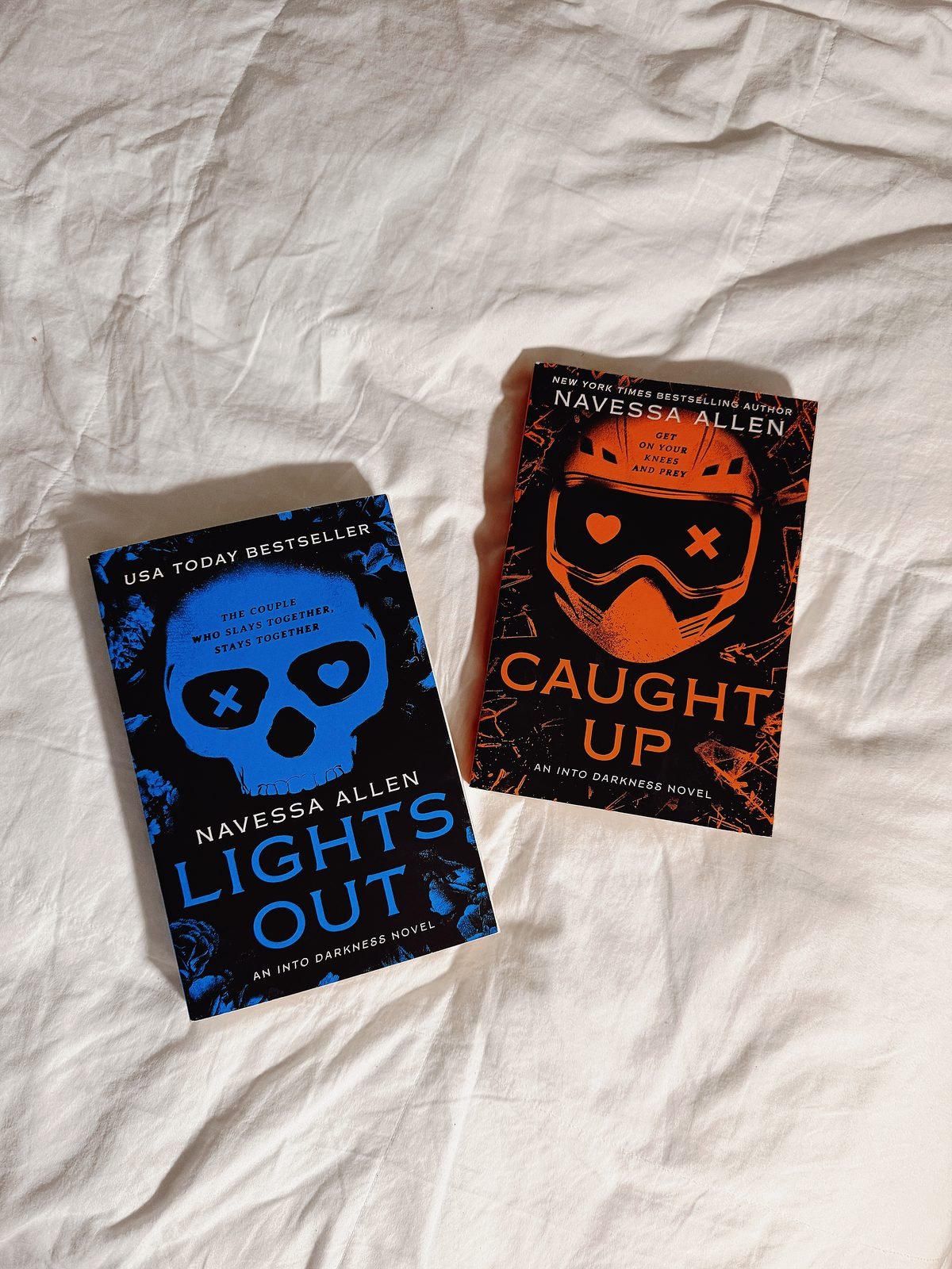 Lights Out and Caught Up by Navessa Allen on a white bed